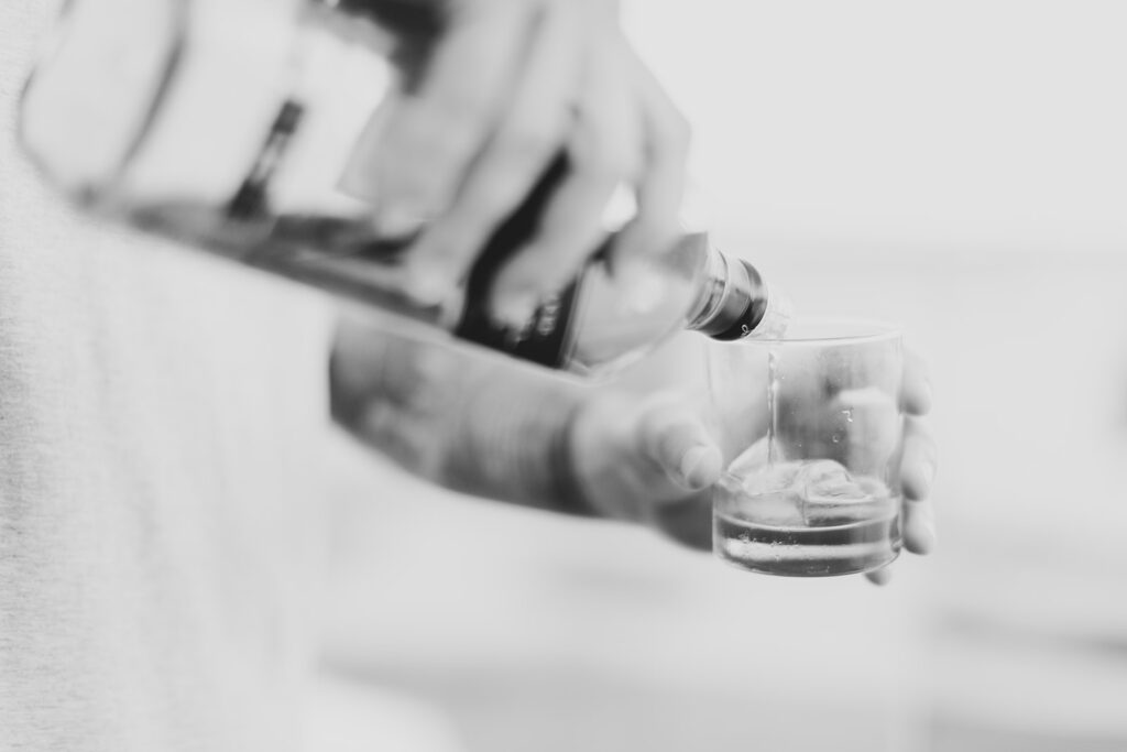 Black and white close-up of the groom pouring a shot while getting ready.