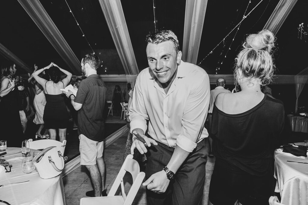 Groom laughing while leaning over a chair during the party.