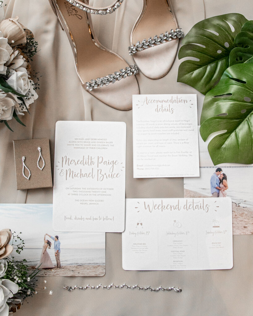 Flatlay of wedding invitation suite, jewelry, and bridal accessories styled with tropical leaves.