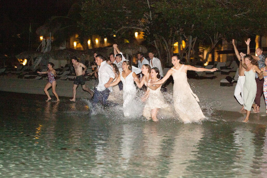 Bride and groom leading their wedding guests into the shallow beach water at night during their Jamaica destination wedding celebration.