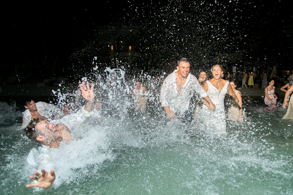 Groom and wedding guests crashing into the water while celebrating during the nighttime ocean dip.