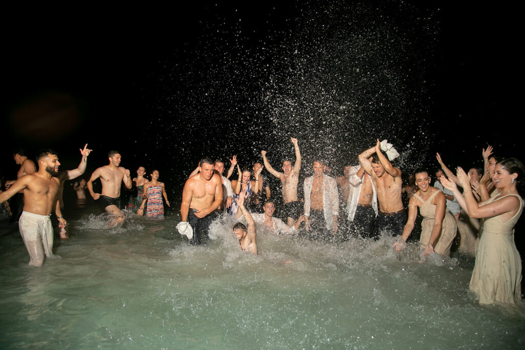 Large group of wedding guests cheering and splashing in the ocean after the reception at the Royalton Negril.
