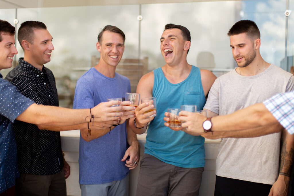 Groom and groomsmen laughing together while raising glasses for a toast.