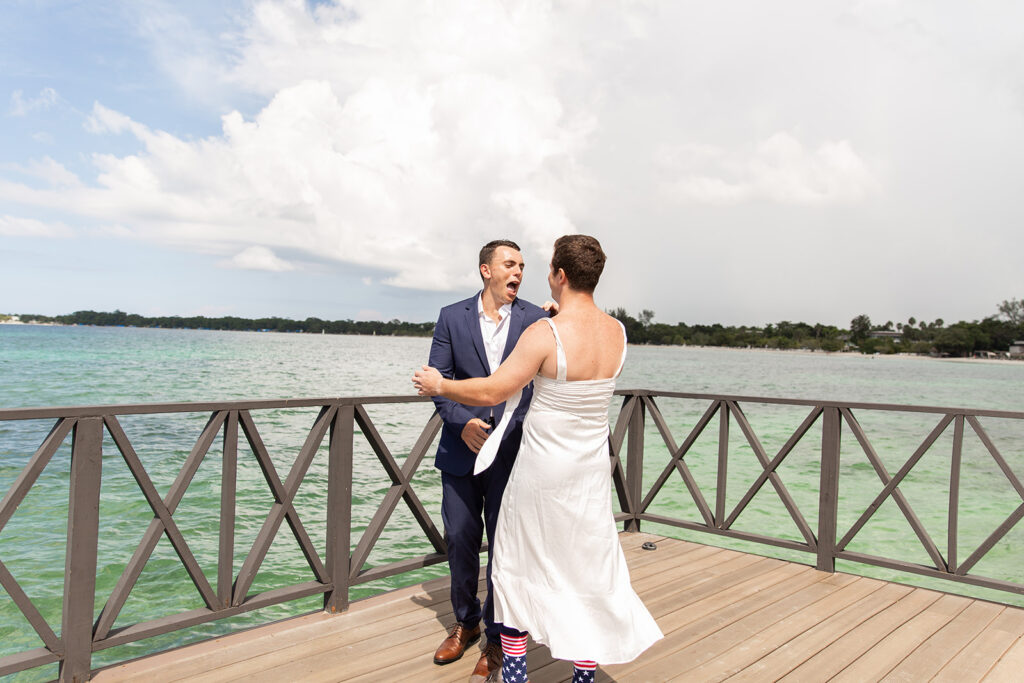 Groom and friend dressed in a wedding gown laughing as they approach each other for the faux first look on the dock.