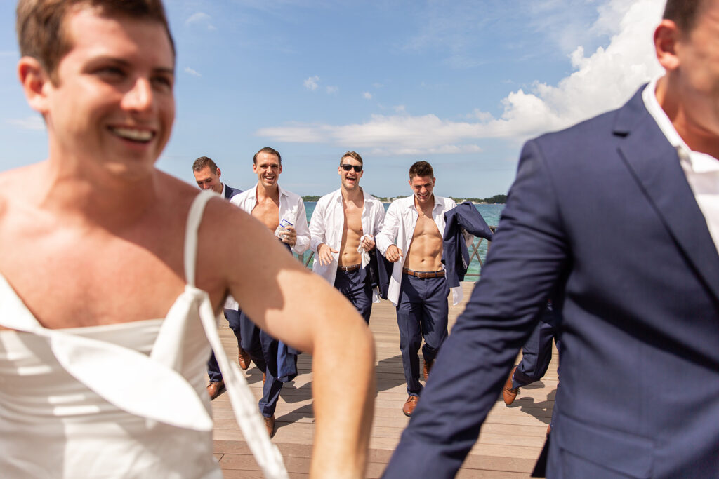 Close-up of the friend in the gown laughing alongside the groom as the bridal party watches.