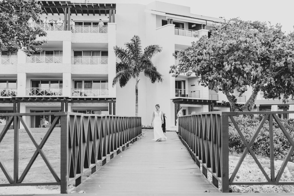 Black and white photo of the bride walking across the dock toward the groom outside the Royalton Negril Resort.
