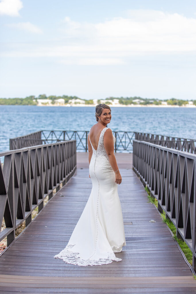 Bride standing on the dock overlooking the ocean, smiling back over her shoulder before the first look.