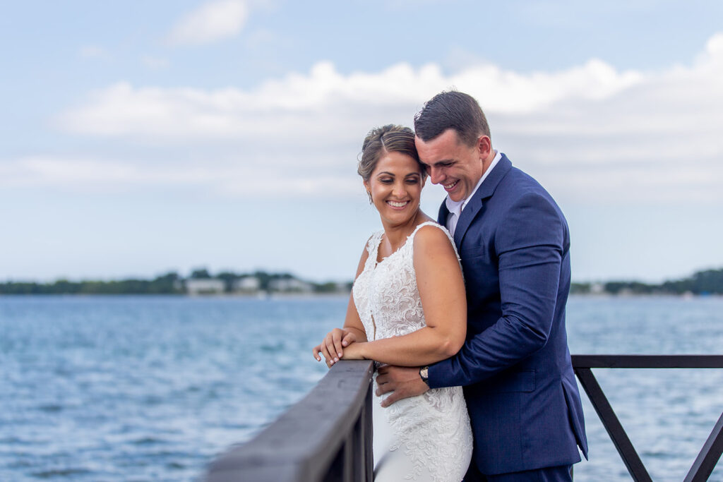 Bride and groom smiling as they stand together along a waterfront railing at Royalton Negril.