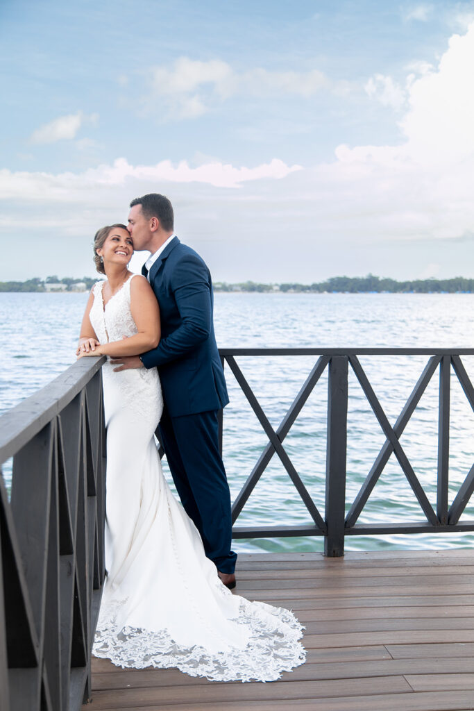 Bride and groom embracing along the boardwalk railing overlooking the sea.