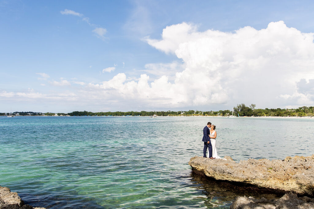 Couple standing together on a rock ledge overlooking the Caribbean Sea.