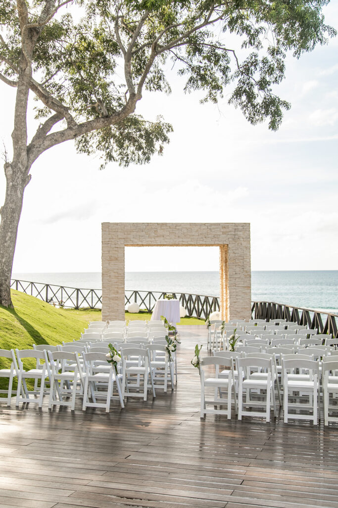 Ceremony setup overlooking the ocean at Royalton Negril with white chairs and a modern stone arch.