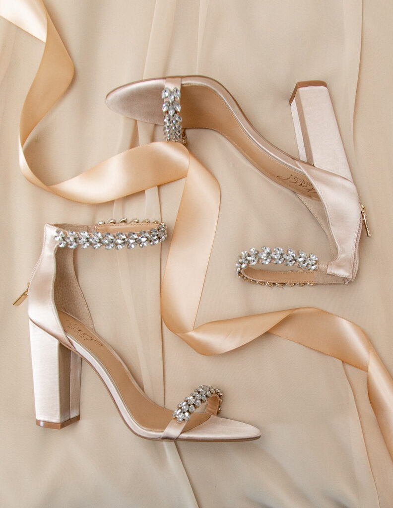 Flatlay of the bride’s pearl-embellished heels styled on soft fabric for wedding detail photos.
