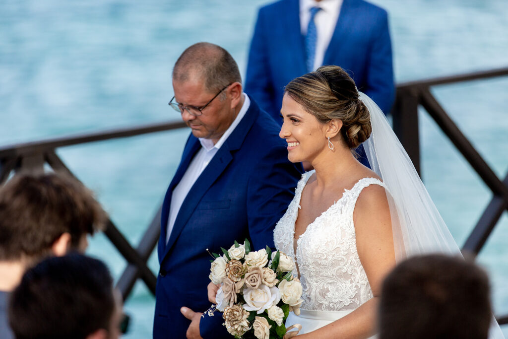 Bride walking down the aisle with her father toward the oceanfront ceremony.