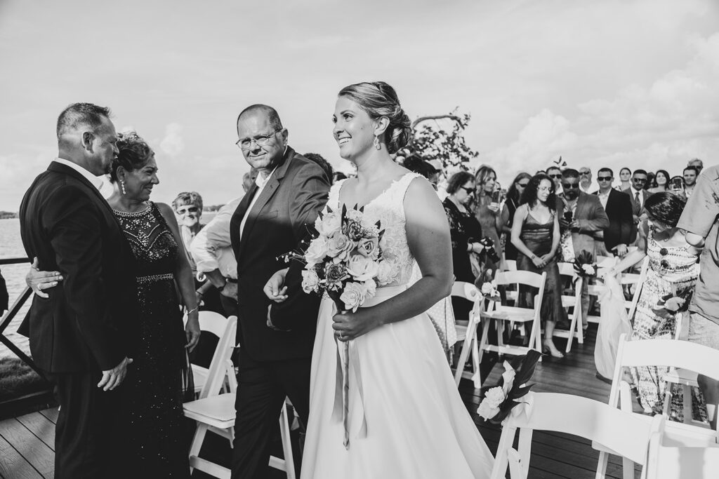 Bride walking down the aisle smiling as guests stand and watch during the ceremony.