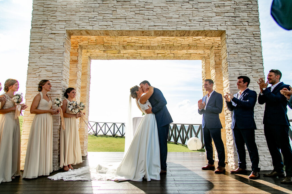 Bride and groom sharing their first kiss under the stone arch at Royalton Negril.