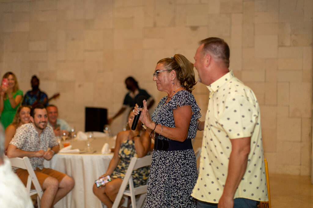 Parents giving a speech with a microphone while guests watch during the welcome reception.