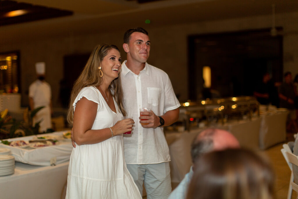 Bride-and-groom-to-be smiling and holding drinks near the buffet area at their welcome reception.