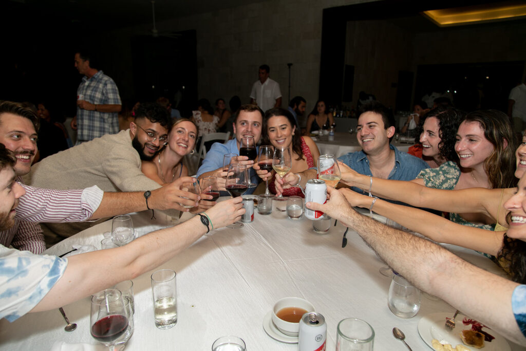 Long table of guests clinking glasses and laughing during the reception dinner.