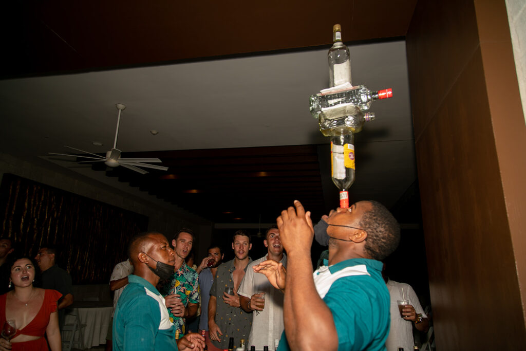 Guests cheering as a resort entertainer balances multiple liquor bottles overhead during the welcome party.