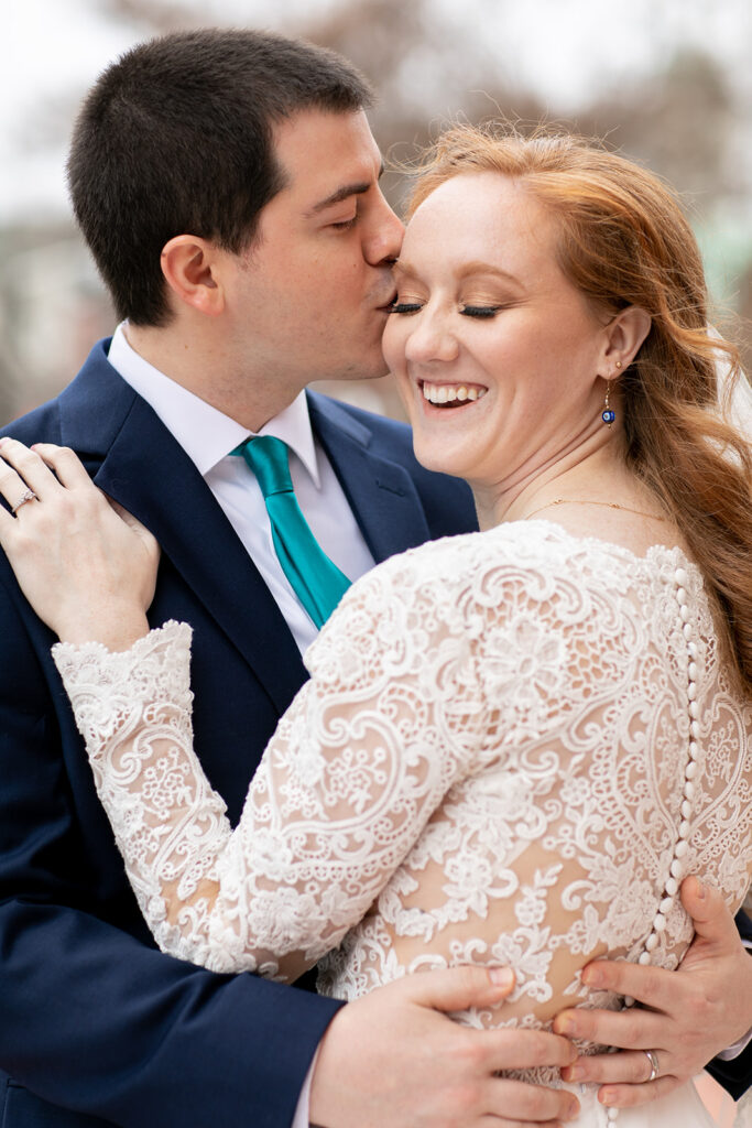 Groom kissing the bride’s temple as she smiles and leans into him during their elopement portraits.