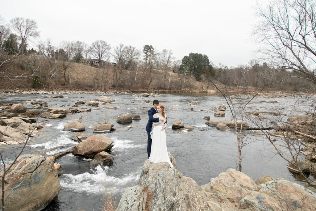Couple posing on a large rock surrounded by river water, holding each other during their elopement portraits.