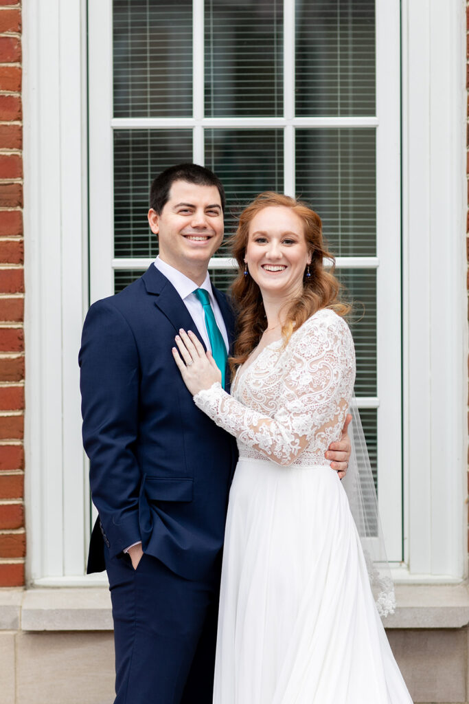 Bride and groom smiling at the camera in front of a tall arched courthouse window.