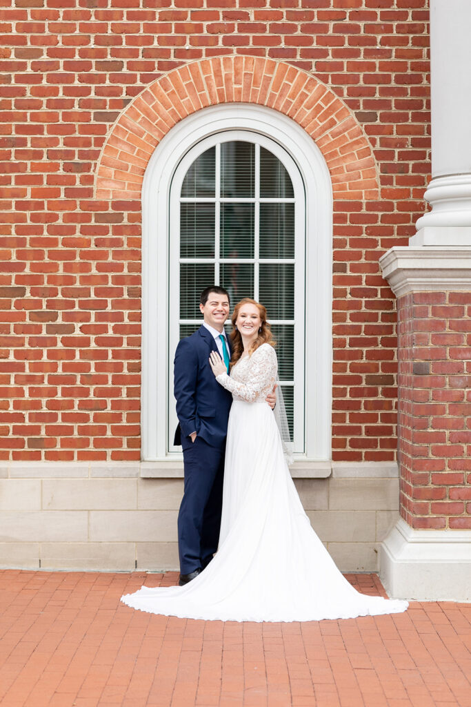 Bride and groom standing beside the arched brick window of the Fredericksburg courthouse.