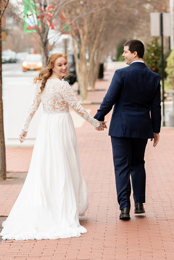 Bride and groom walking toward the camera on a winter day, smiling as they hold hands.