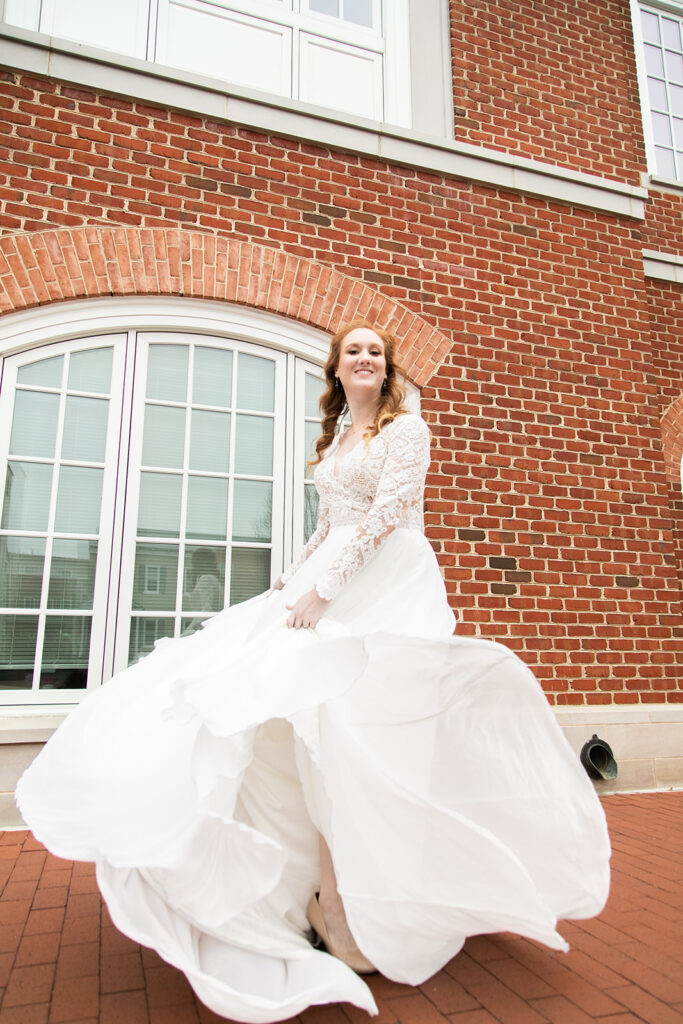 Bride twirling her dress beside a brick building, smiling toward the camera.