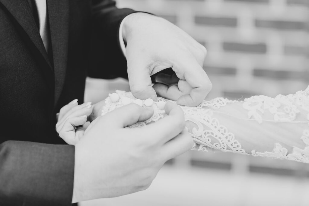 Close-up of groom fastening the bride’s lace sleeve buttons.