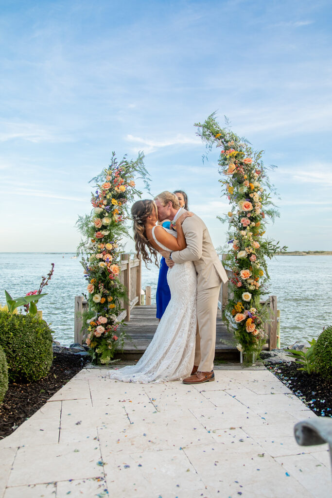 Joyful first kiss during Sarah and Michael’s Ocean City MD backyard beach wedding overlooking the bay
