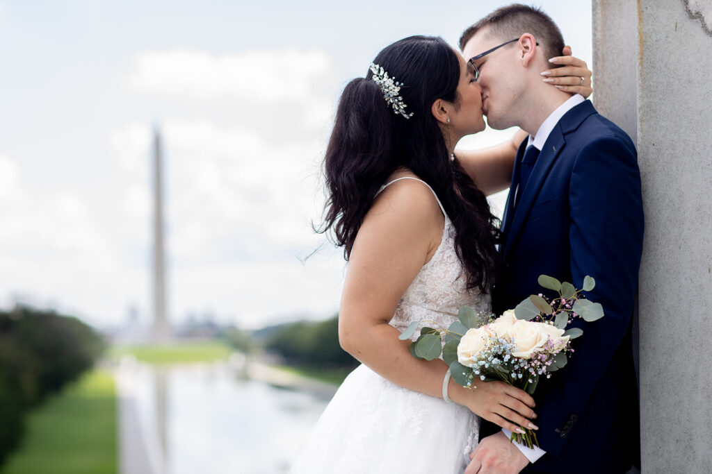 Bride and groom kissing during DC War Memorial elopement with the Washington Monument in the background