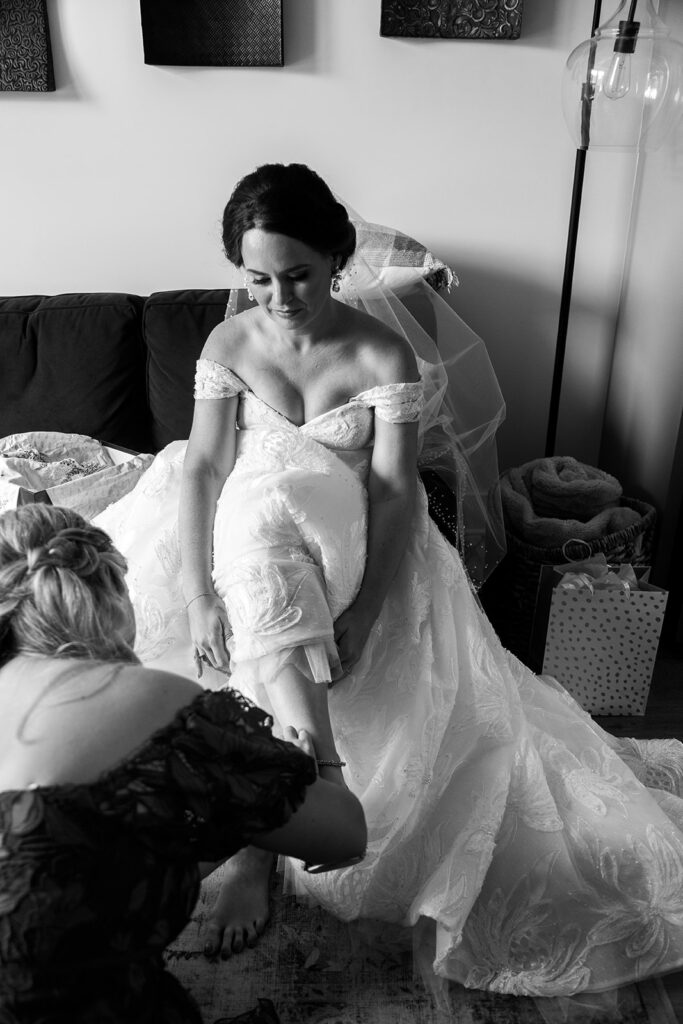 Bride sitting as loved ones adjust her wedding dress during getting ready at an intimate Alexandria wedding.