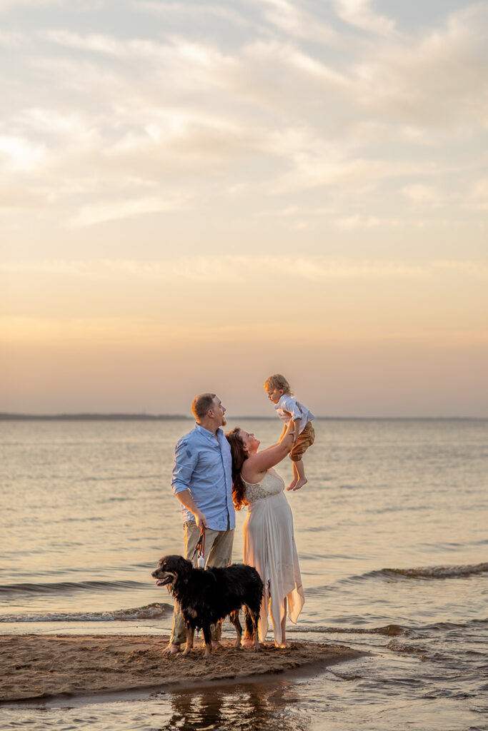Hope and Tyler standing by the water at Terrapin Nature Park at sunset with their dog nearby, capturing soft beach tones and Bay Bridge views.