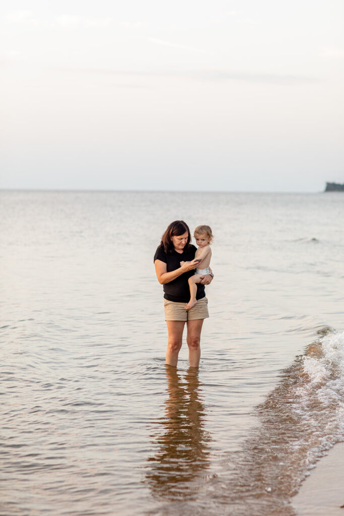 Hope and Tyler’s child being held by his grandmother while standing in the shallow water at Terrapin Nature Park during the engagement session.