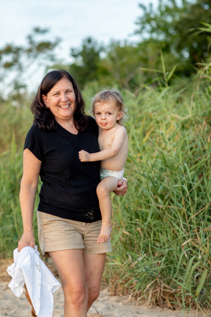 Grandmother holding Hope and Tyler’s child along a grassy path at Terrapin Nature Park during their engagement session.