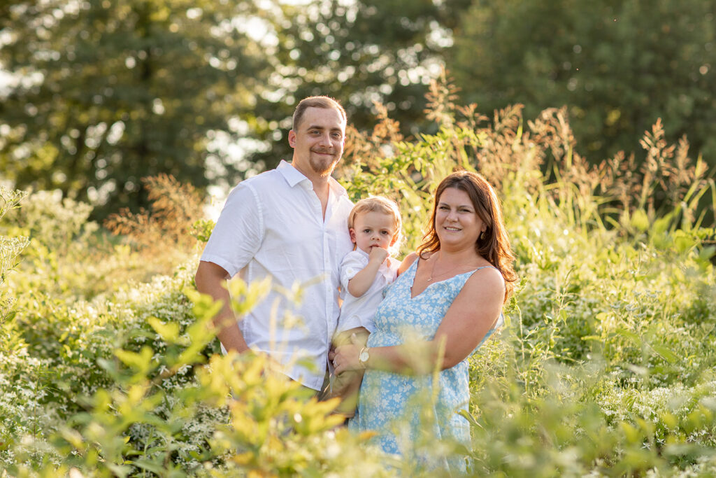 Hope and Tyler holding their son during their Terrapin Nature Park engagement session, standing in yellow wildflowers with warm golden light.