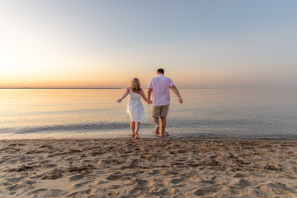 Playful beach engagement photos near DC of a couple walking into the water at Terrapin Nature Park