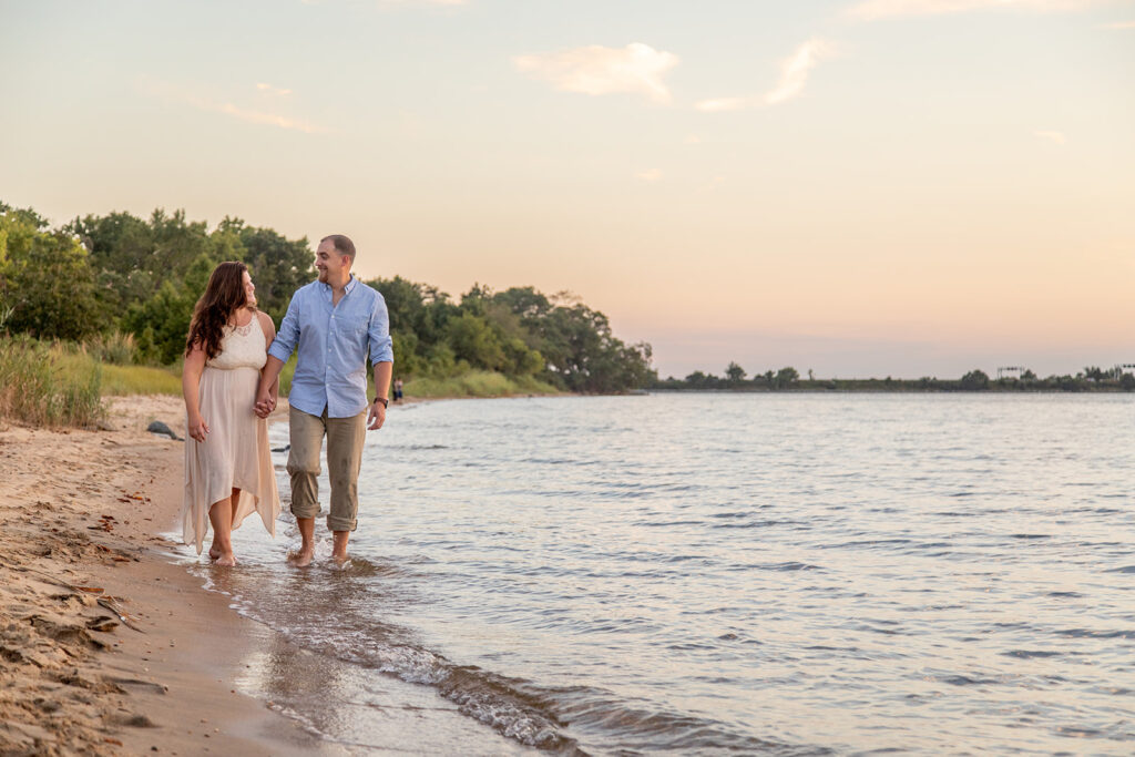 Hope and Tyler walking barefoot along the waterline at Terrapin Nature Park during their engagement session.