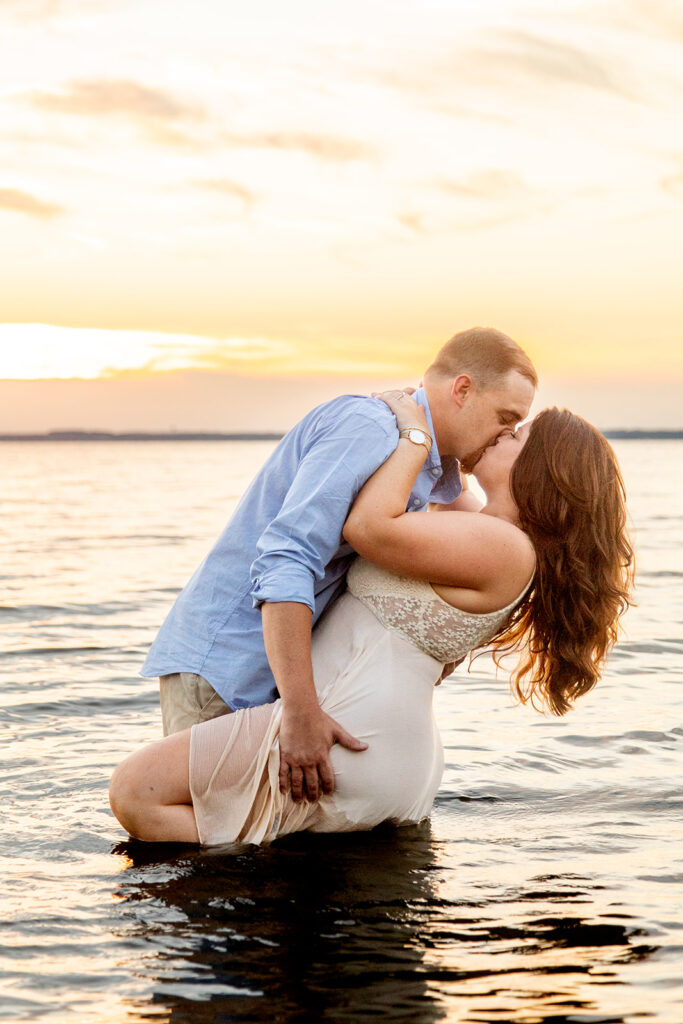 Hope and Tyler kissing while he lifts her in the shallow water at Terrapin Nature Park at sunset.