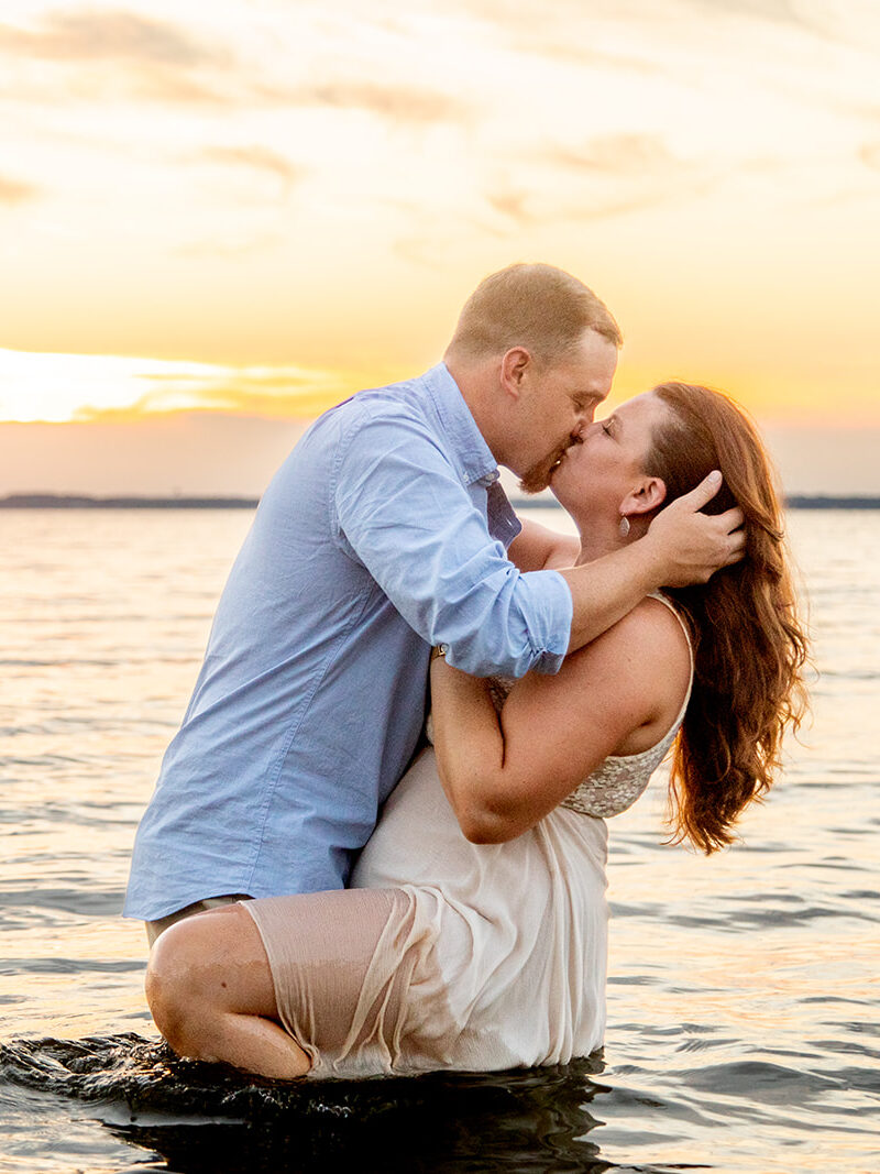 Hope and Tyler kissing in the shallow water as the sunset glows behind them at Terrapin Nature Park.