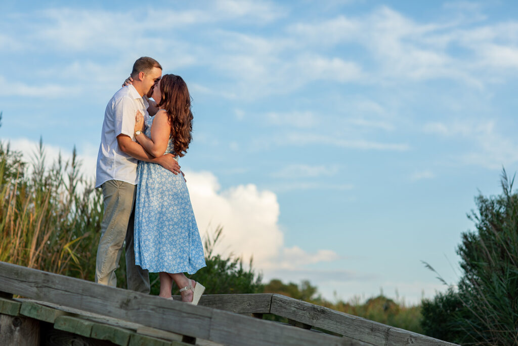 Hope and Tyler standing together on driftwood with bright blue skies at Terrapin Nature Park during their engagement session.